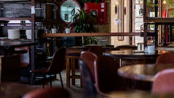 Interior acogedor de restaurante con mesas y sillas de madera, un cuadro eléctrico rojo y un espejo grande en la pared.