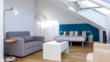 Una habitación moderna estilo loft, con techo inclinado, un sofá gris, una mesa de centro blanca, cama con paredes de acento azul y un tragaluz.