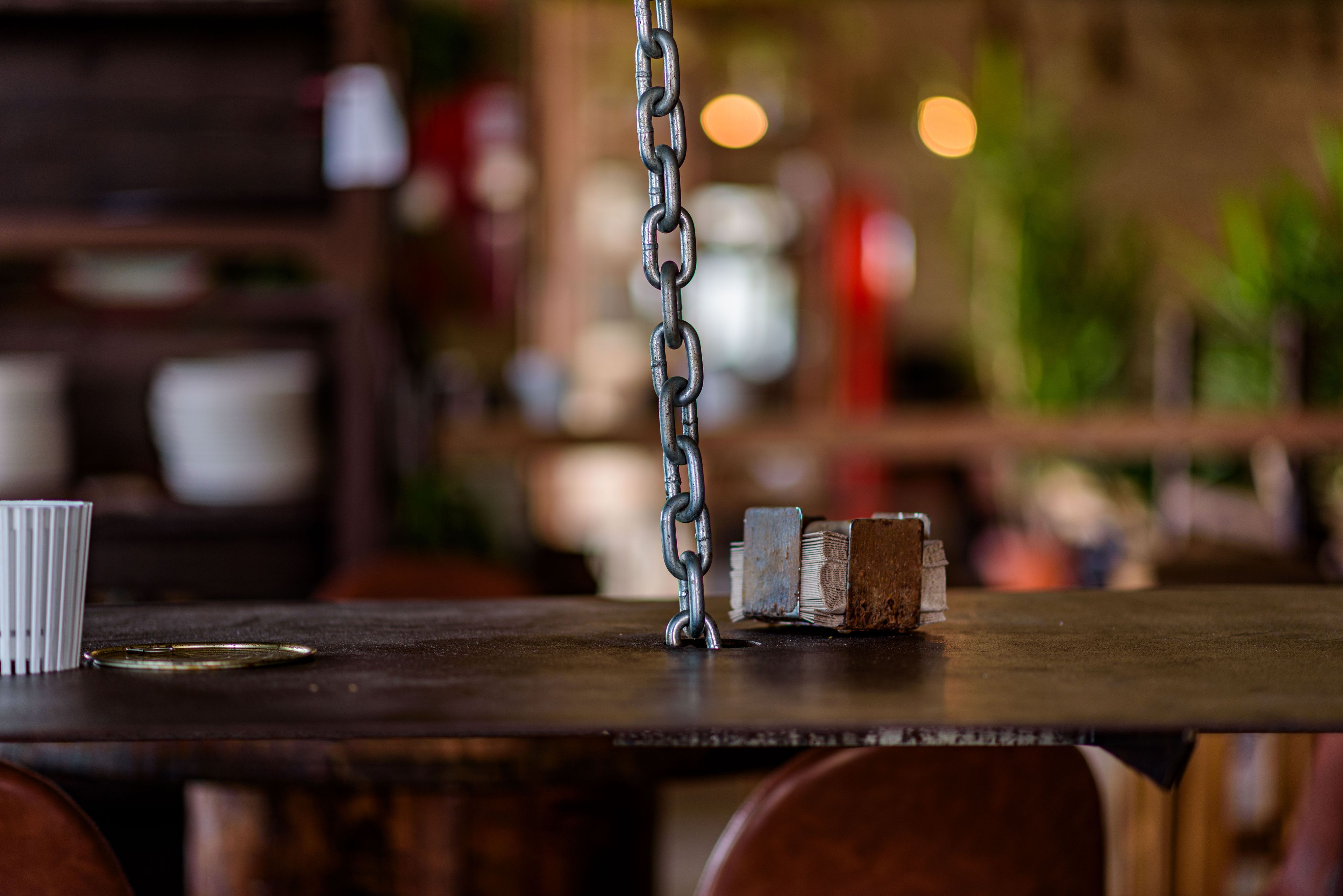 A wooden table with a metal chain, a white cup, and a brush.