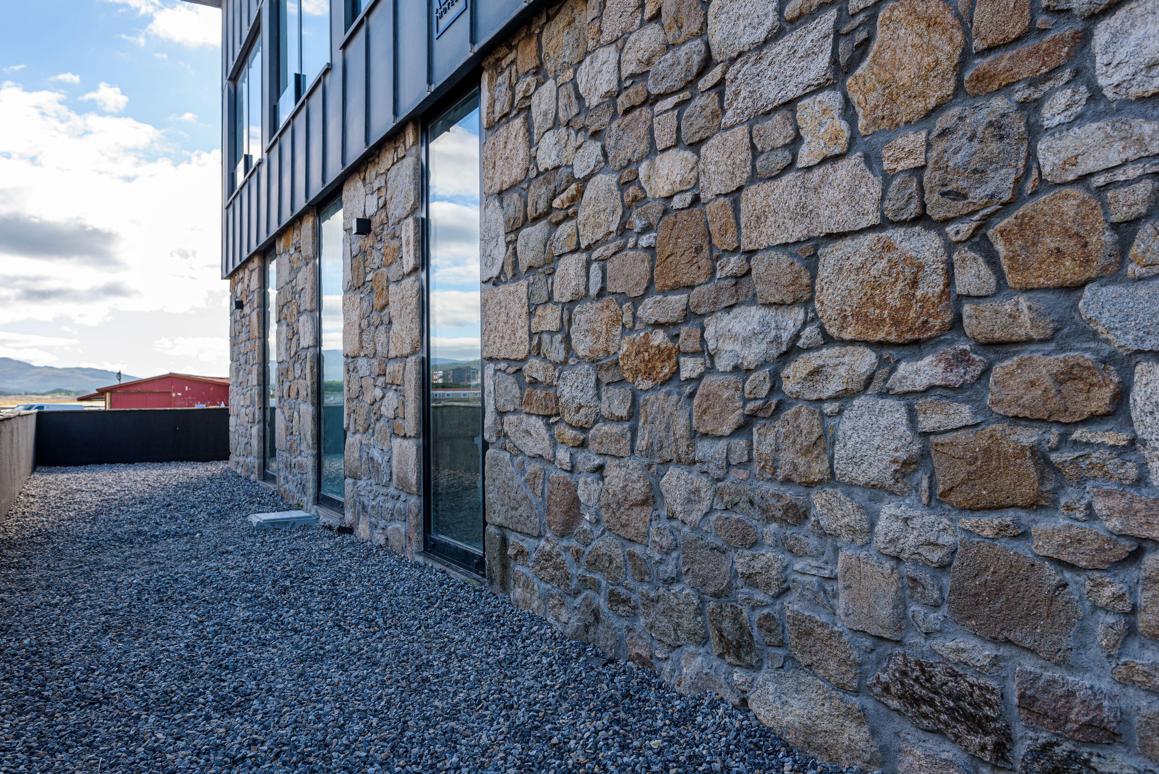 A stone building with large windows and a gravel ground.