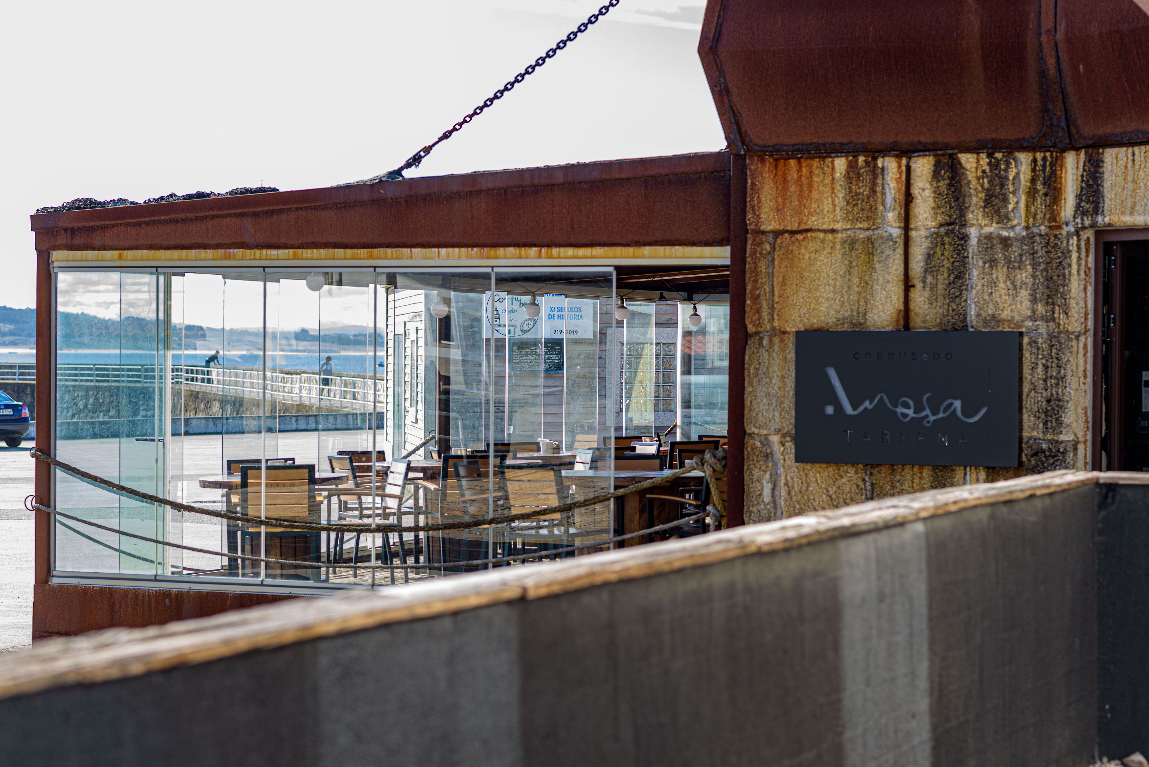 A restaurant with outdoor seating overlooking a body of water, featuring a rustic stone wall and a sign with the name 'Luzosa'.