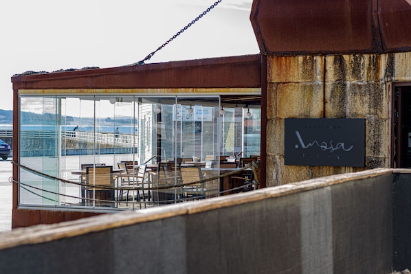 A restaurant with outdoor seating overlooking a body of water, featuring a rustic stone wall and a sign with the name 'Luzosa'. - Alda Corrubedo (Ribeira)
