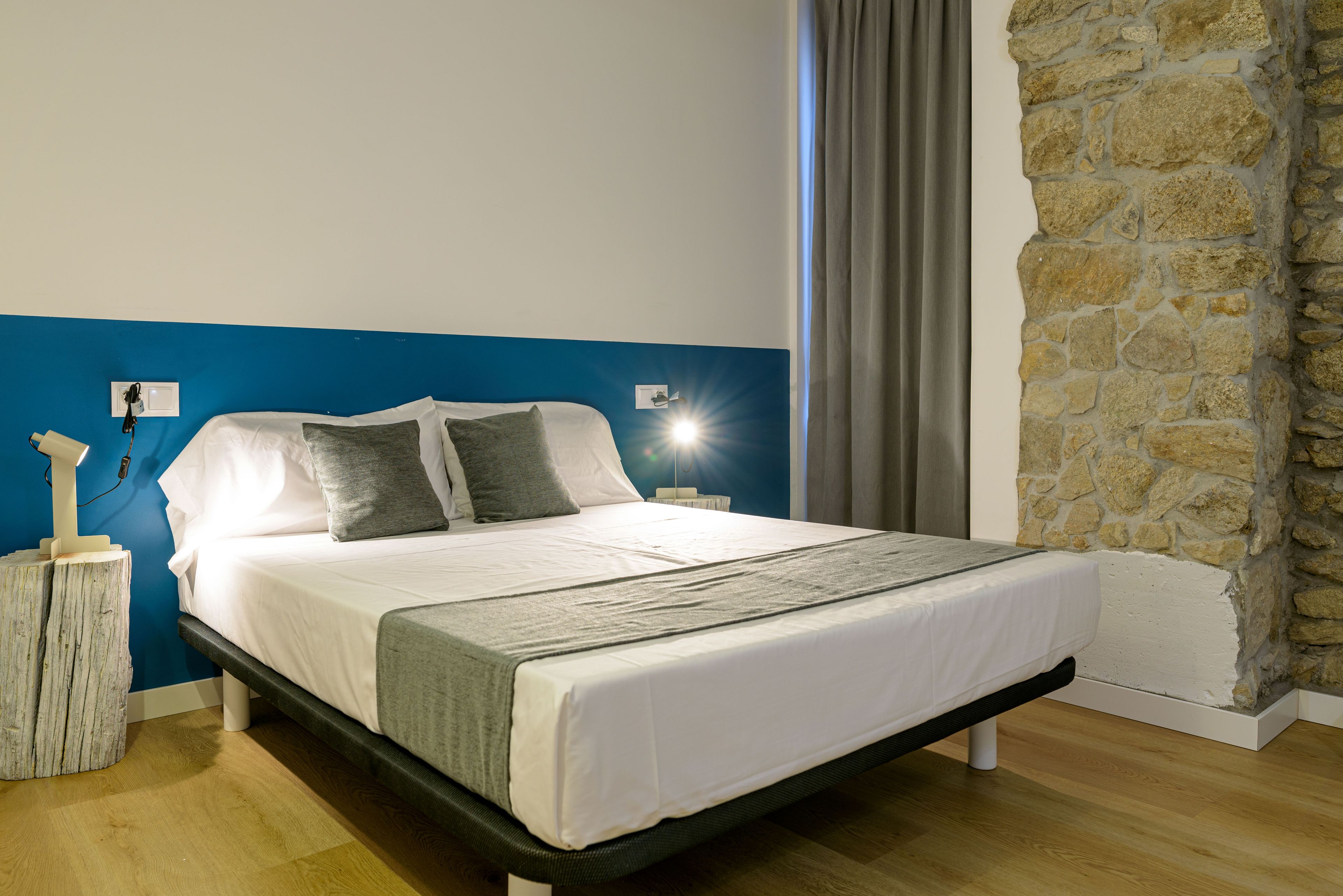 A bed with white bedding, a stone wall, and a blue accent wall.
