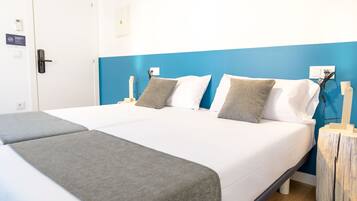 Habitación de hotel con una cama grande, dos mesitas de noche, un buró, una puerta y un teléfono instalado en la pared.