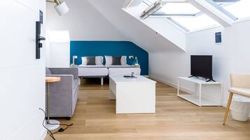 Un dormitorio moderno estilo loft con tragaluces, cama, televisor y zona de estar con sofá y sillón.