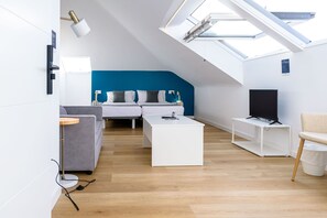 A modern loft-style bedroom with a skylight, a bed, a TV, and a seating area with a sofa and armchair. - Alda Corrubedo (Ribeira)