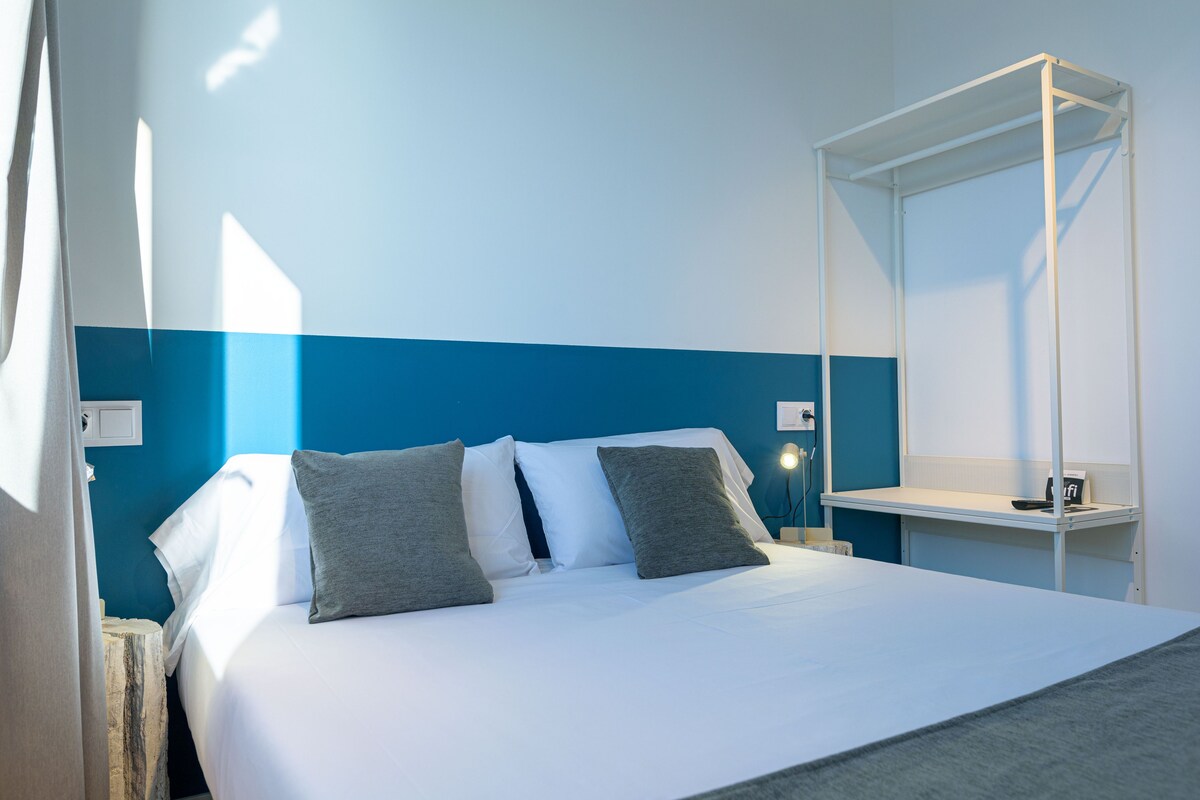 A hotel room with a bed, a nightstand, a bedside table, and a mirror.