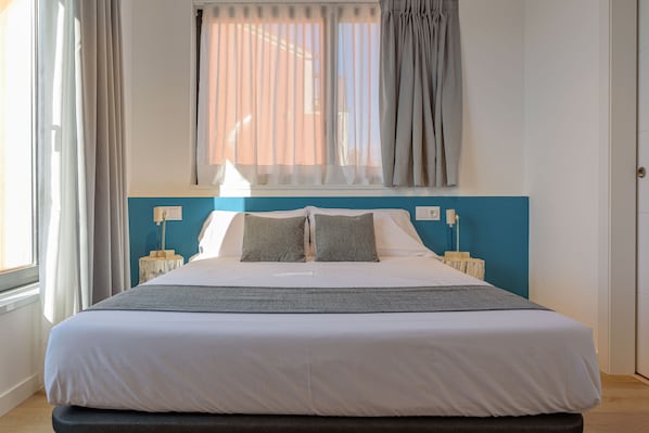 A neatly made bed with white linens and two pillows, a bedside table with a lamp, and a window with curtains. - Alda Corrubedo (Ribeira)