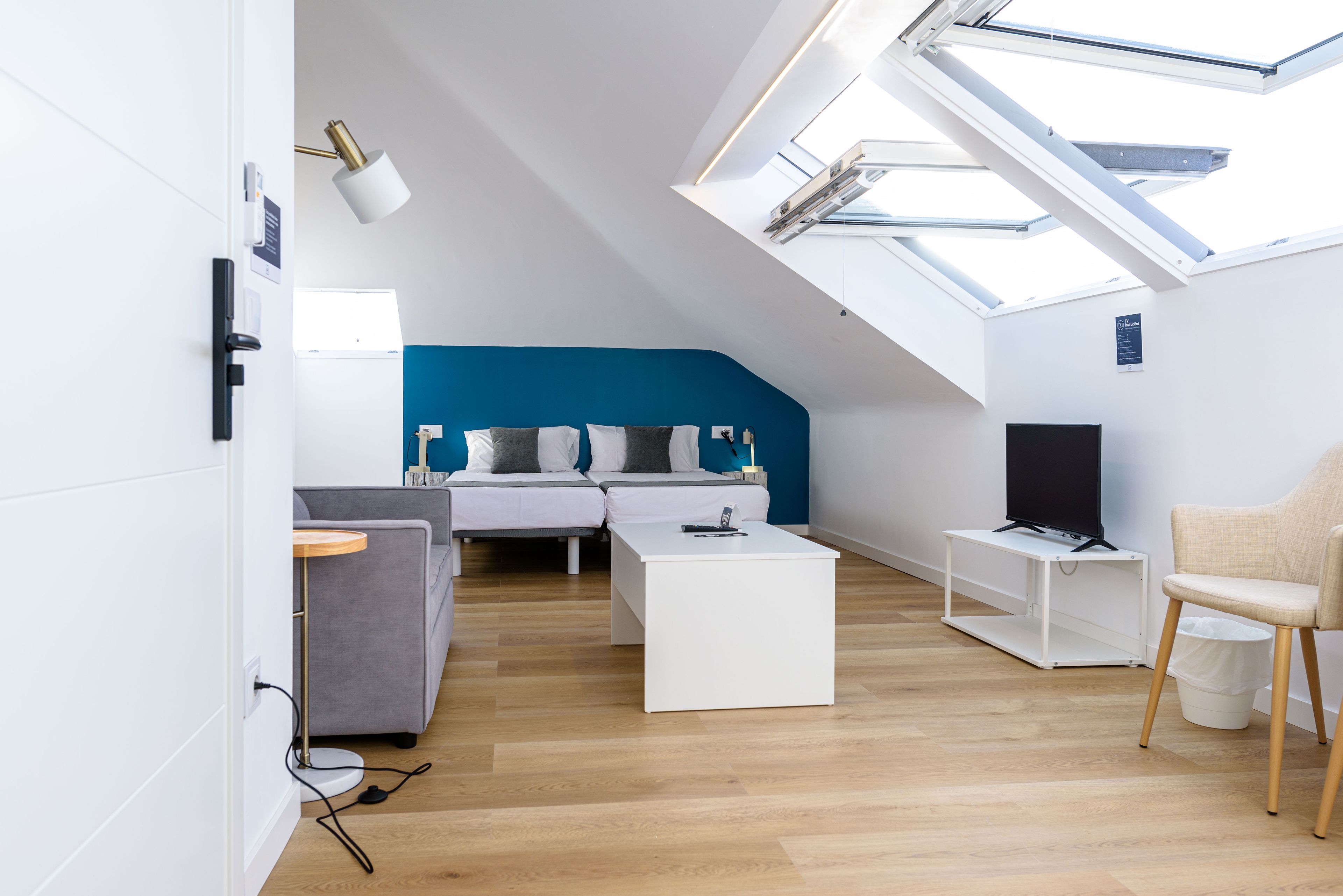 Una sala de estar moderna con tragaluz, un sofá gris, una mesa de centro blanca y un televisor sobre un mueble.
