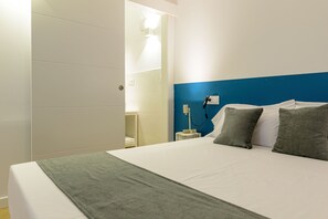 A hotel room with a bed, a nightstand, a lamp, and a bathroom visible through an open door.