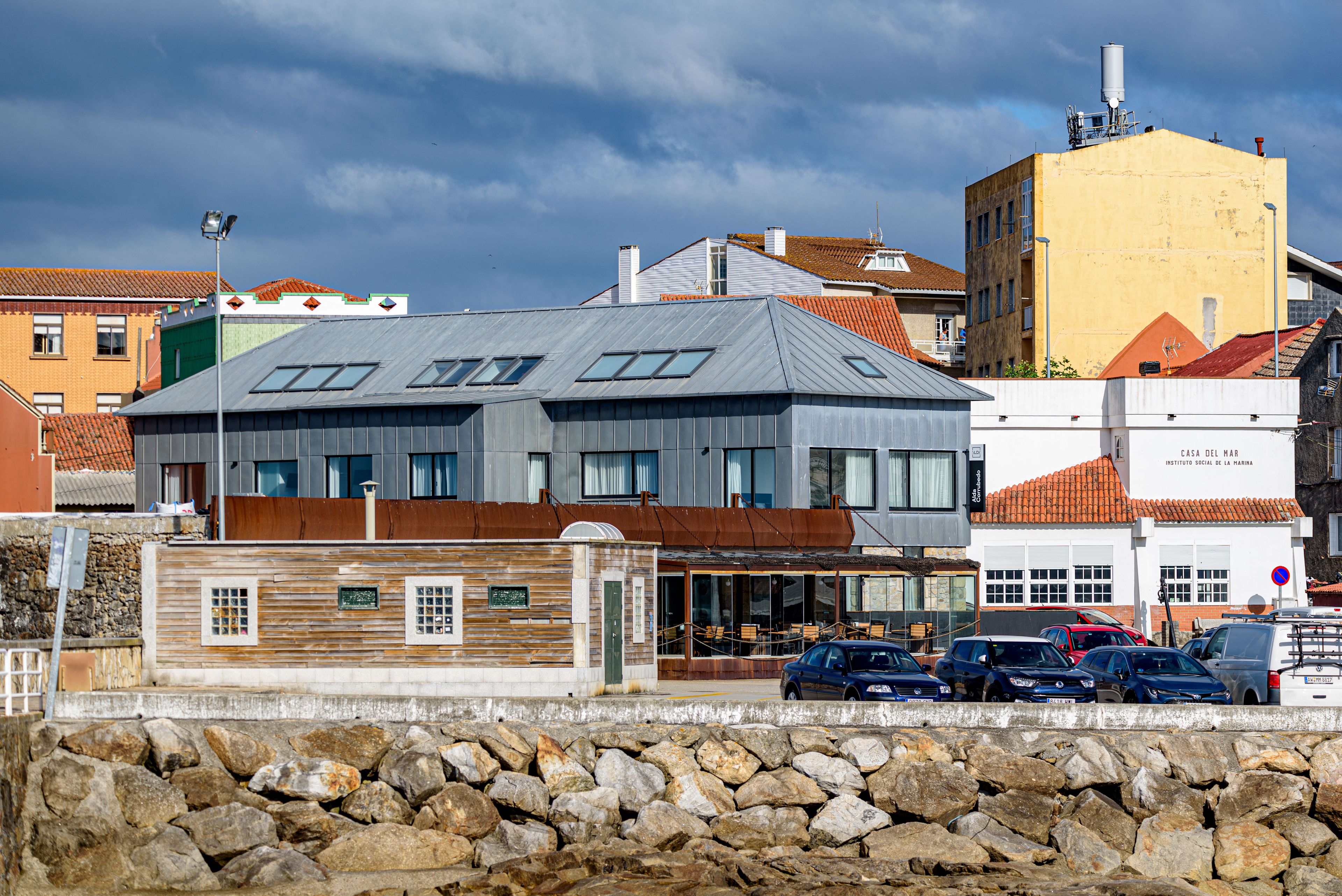 Un bâtiment moderne doté d’un toit plat, de grandes fenêtres et d’un mur en pierre en premier plan.