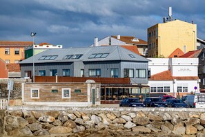 A modern building with a flat roof, large windows, and a stone wall in the foreground. - Alda Corrubedo (Ribeira)