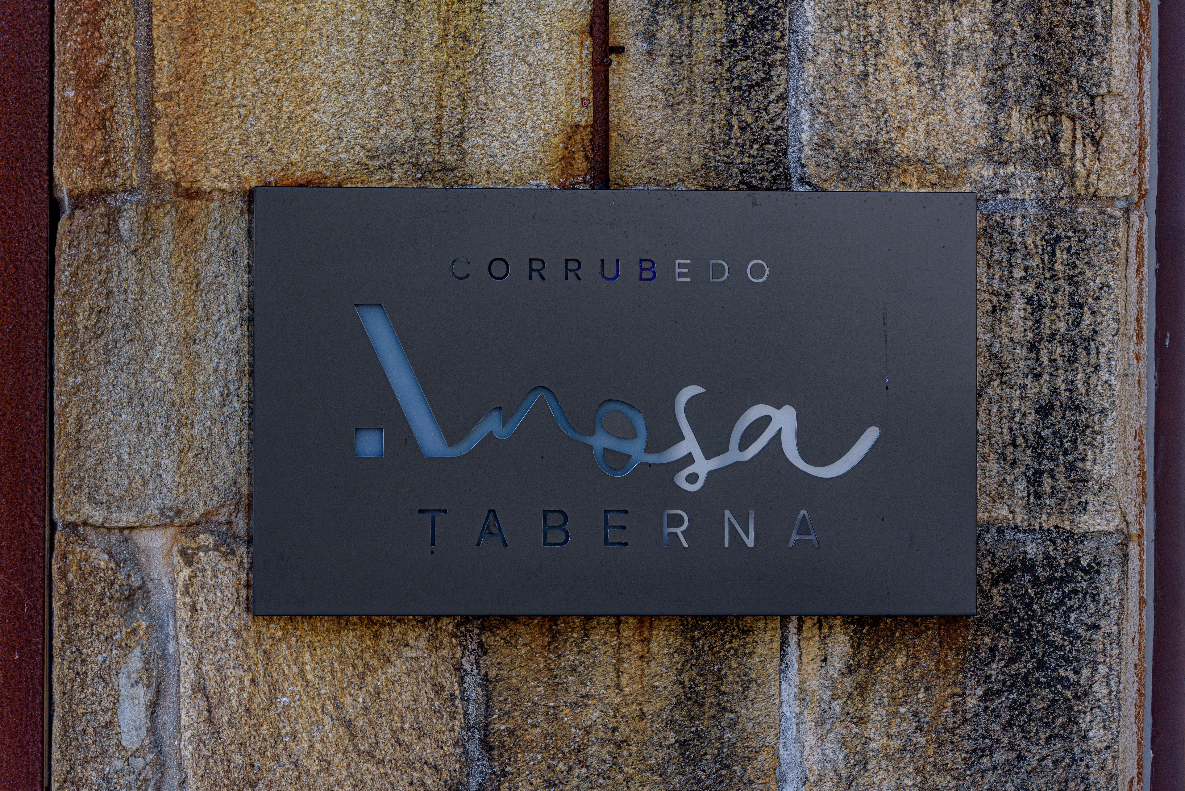 Una señal con el nombre 'CORRUBEDO' y 'TABERNA' en una pared de piedra.