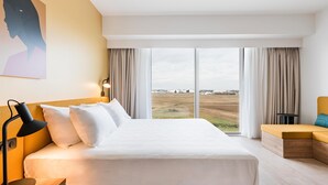 Une chambre d’hôtel moderne, dotée d’un grand lit, d’un bureau, d’une chaise et offrant une vue sur la campagne.