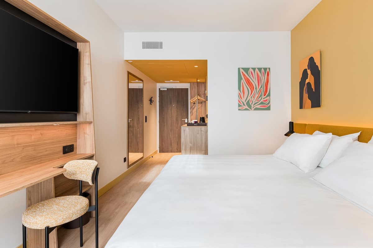 Een hotelkamer met een bed, een televisie, een bureau met stoel, en een spiegel.