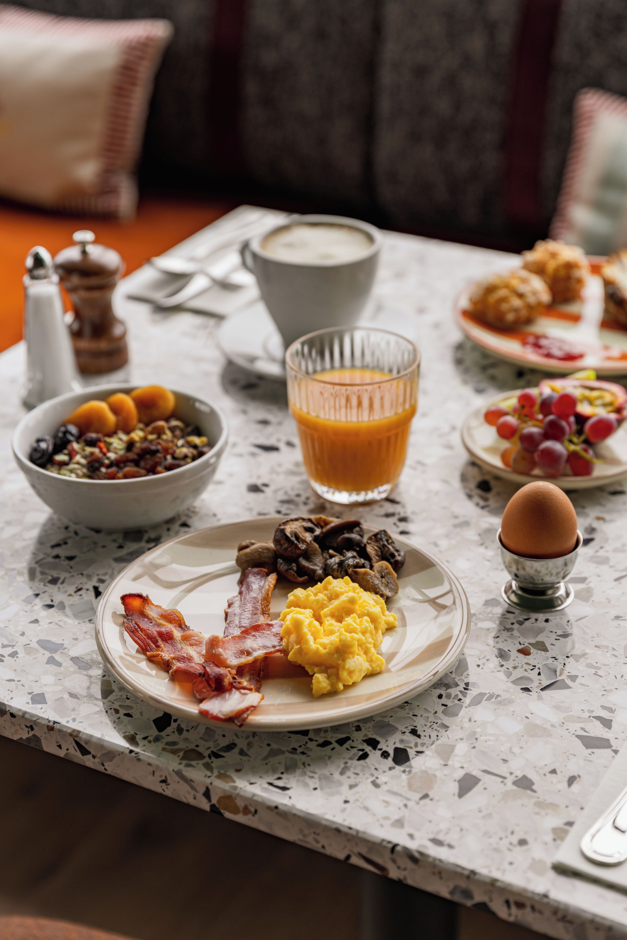A breakfast table with various food items and a glass of orange juice.