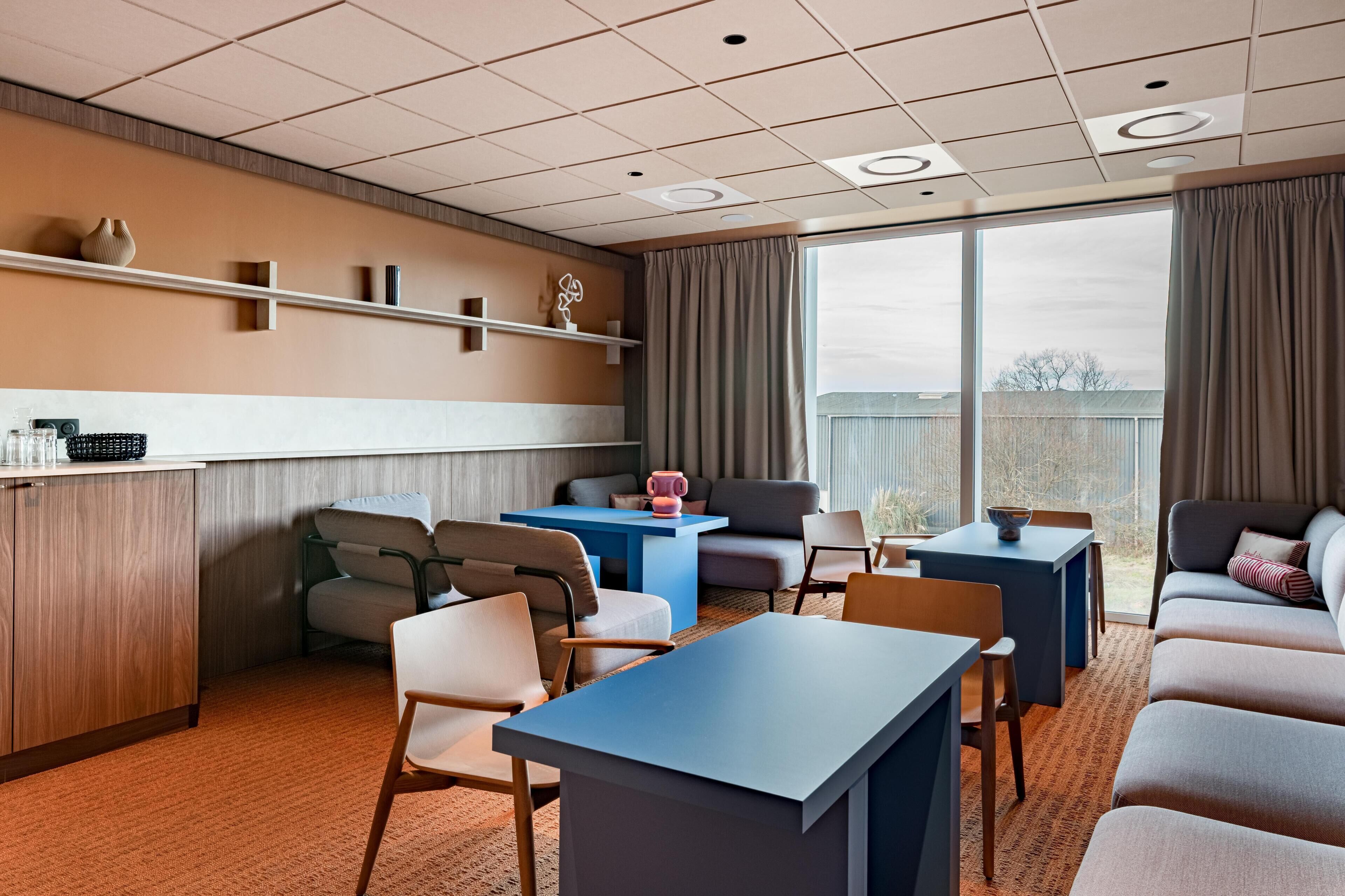 Et moderne hotelværelse med spiseplads, en sofa og et stort vindue med gardiner.