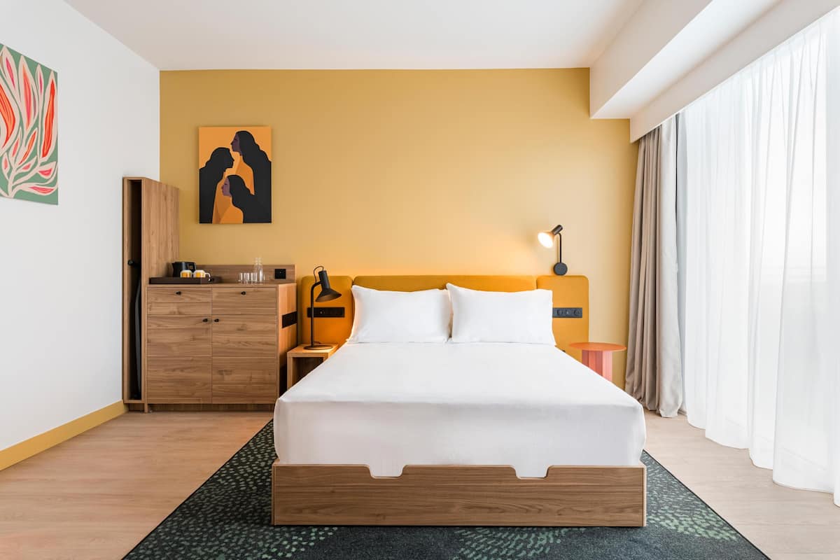 Een hotelkamer met een bed, een nachtkastje, een lamp, een houten dressoir en een schilderij aan de muur.
