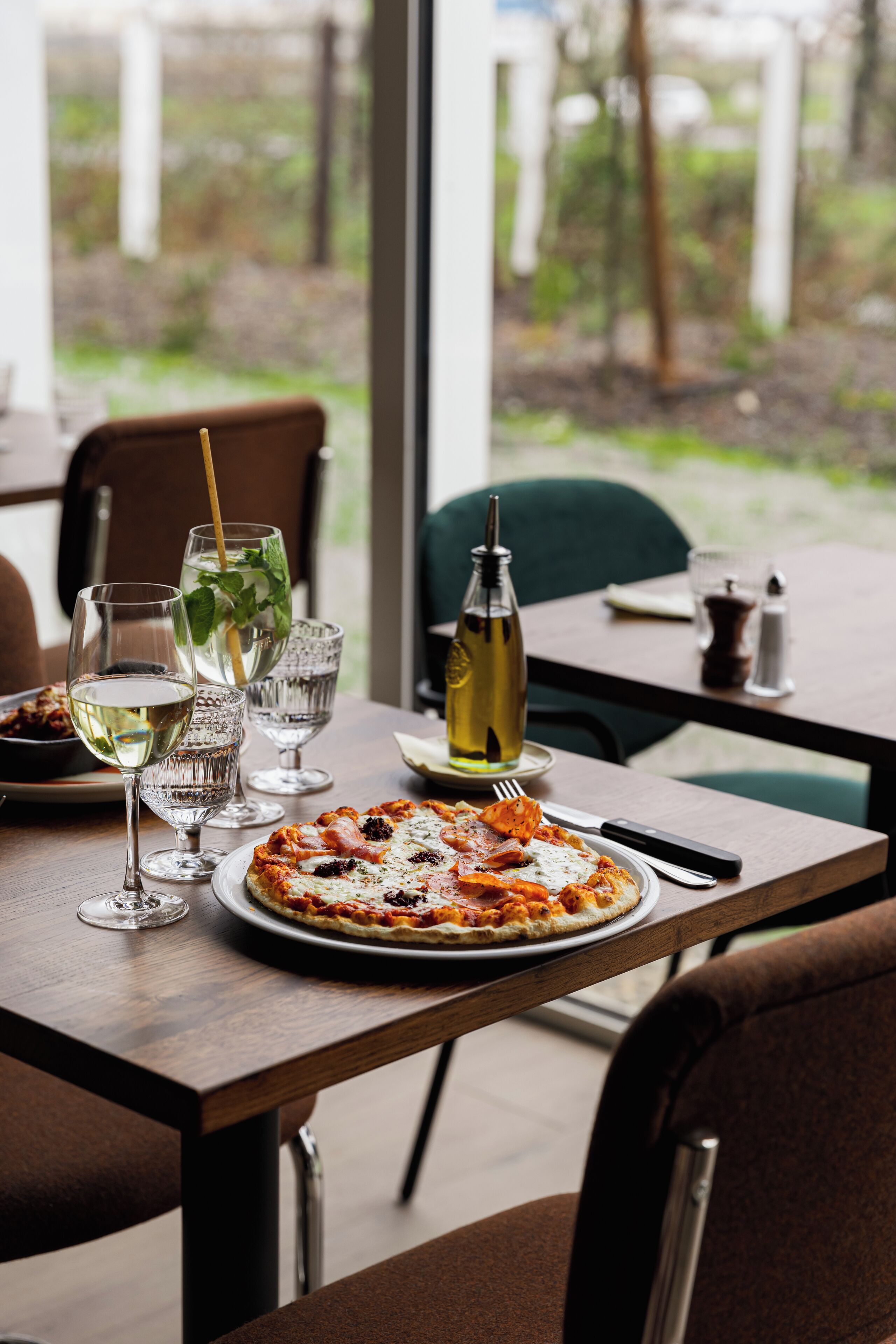 A dining table with a pizza, wine glasses, and a bottle of olive oil.