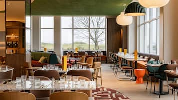 Een modern restaurant met hoge plafonds, grote ramen en diverse zitmogelijkheden.