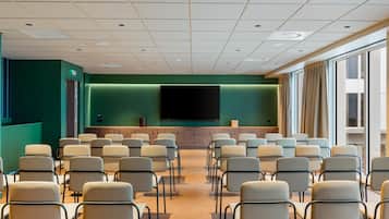 A conference room with rows of chairs, a large flat-screen TV, and a green accent wall.
