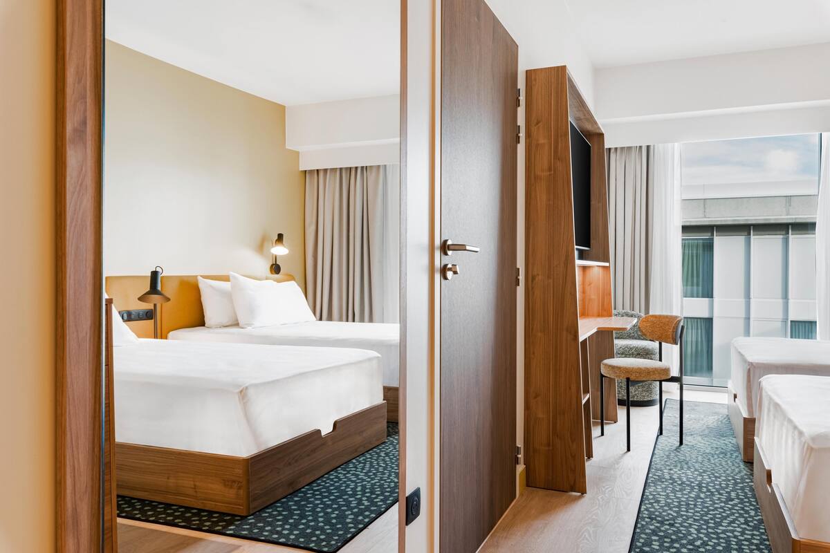 Een hotelkamer met twee bedden, een bureau, een stoel en uitzicht op buiten.