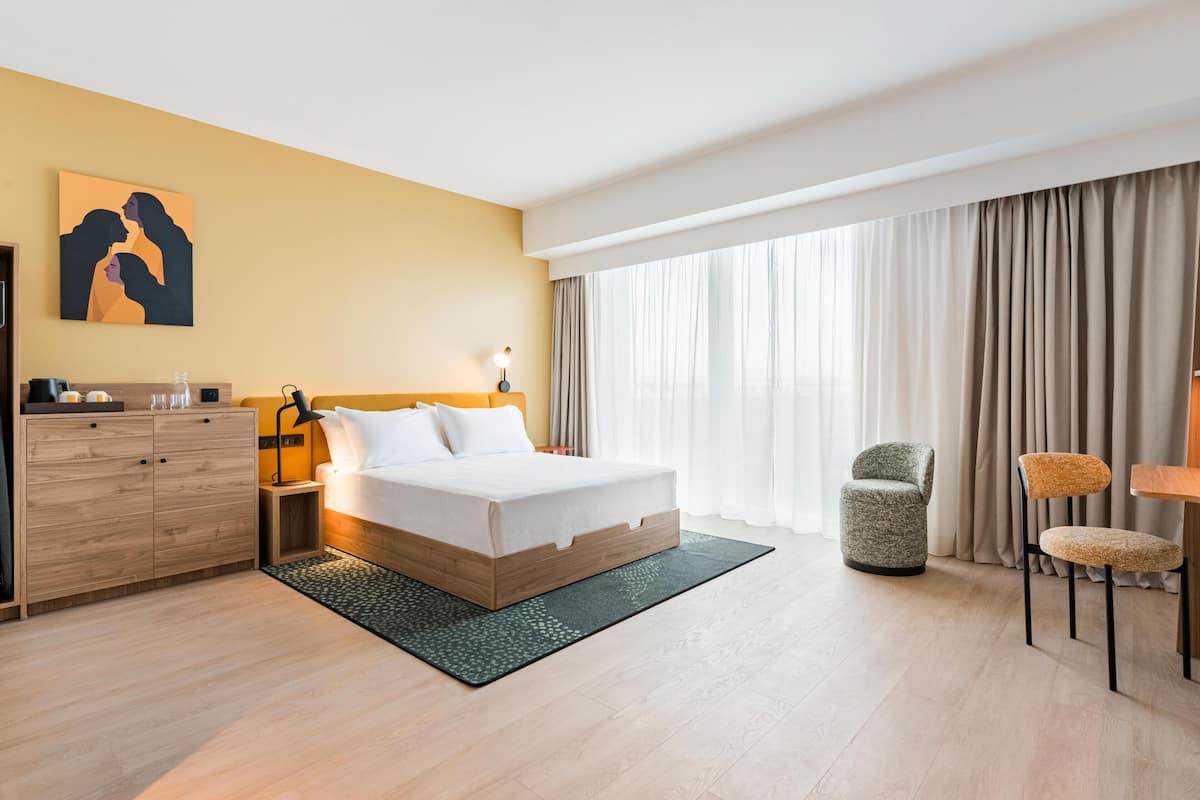 Een hotelkamer met een bed, een bureau, een stoel, een kledingkast en een schilderij aan de muur.