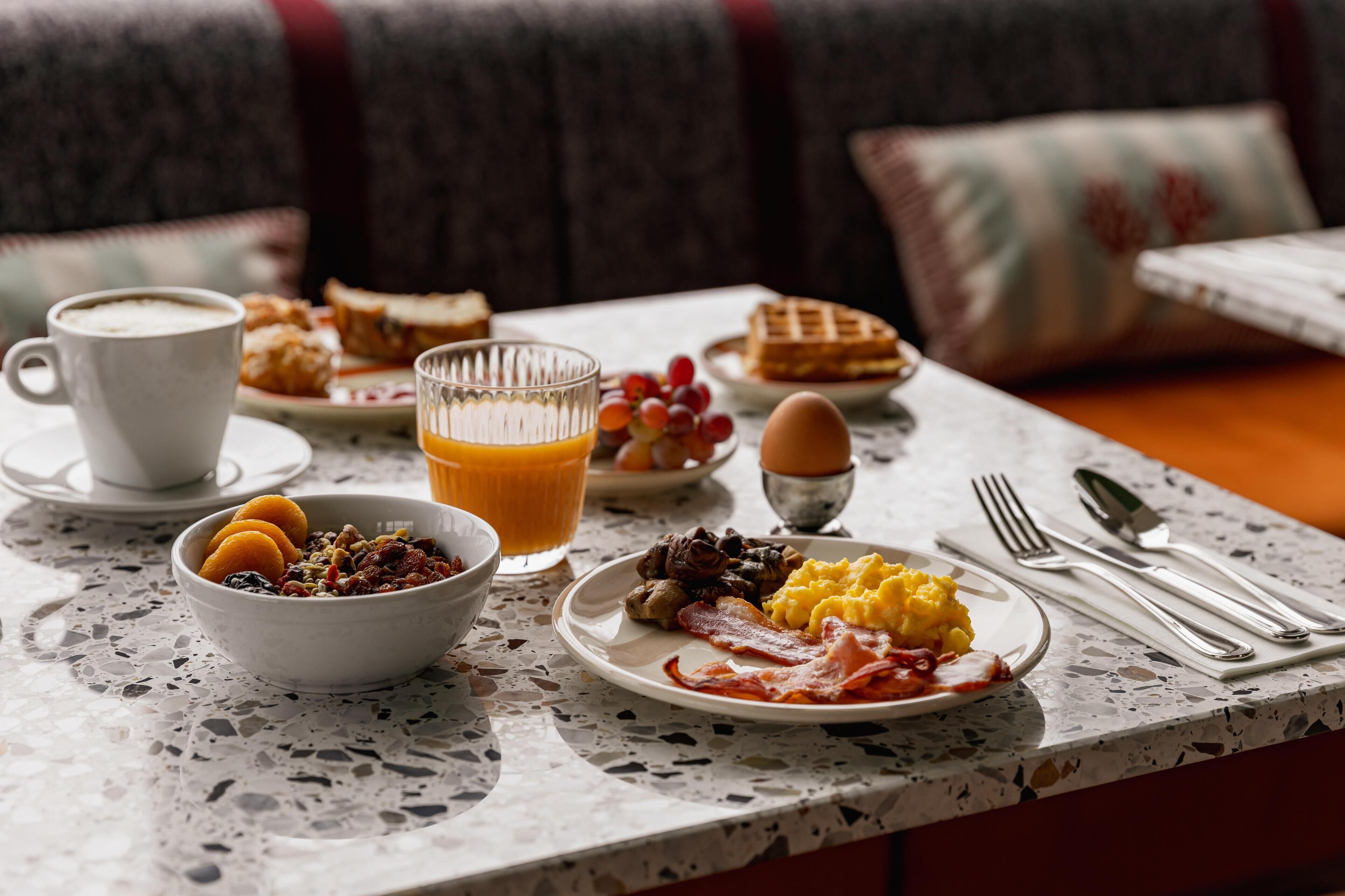 Una mesa de desayuno con diversos platos, una taza de café y un vaso de zumo de naranja.