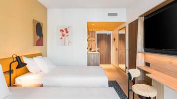 Une chambre d’hôtel moderne équipée d’un lit, d’un bureau, d’une télévision et ornée d’œuvres d’art sur les murs.