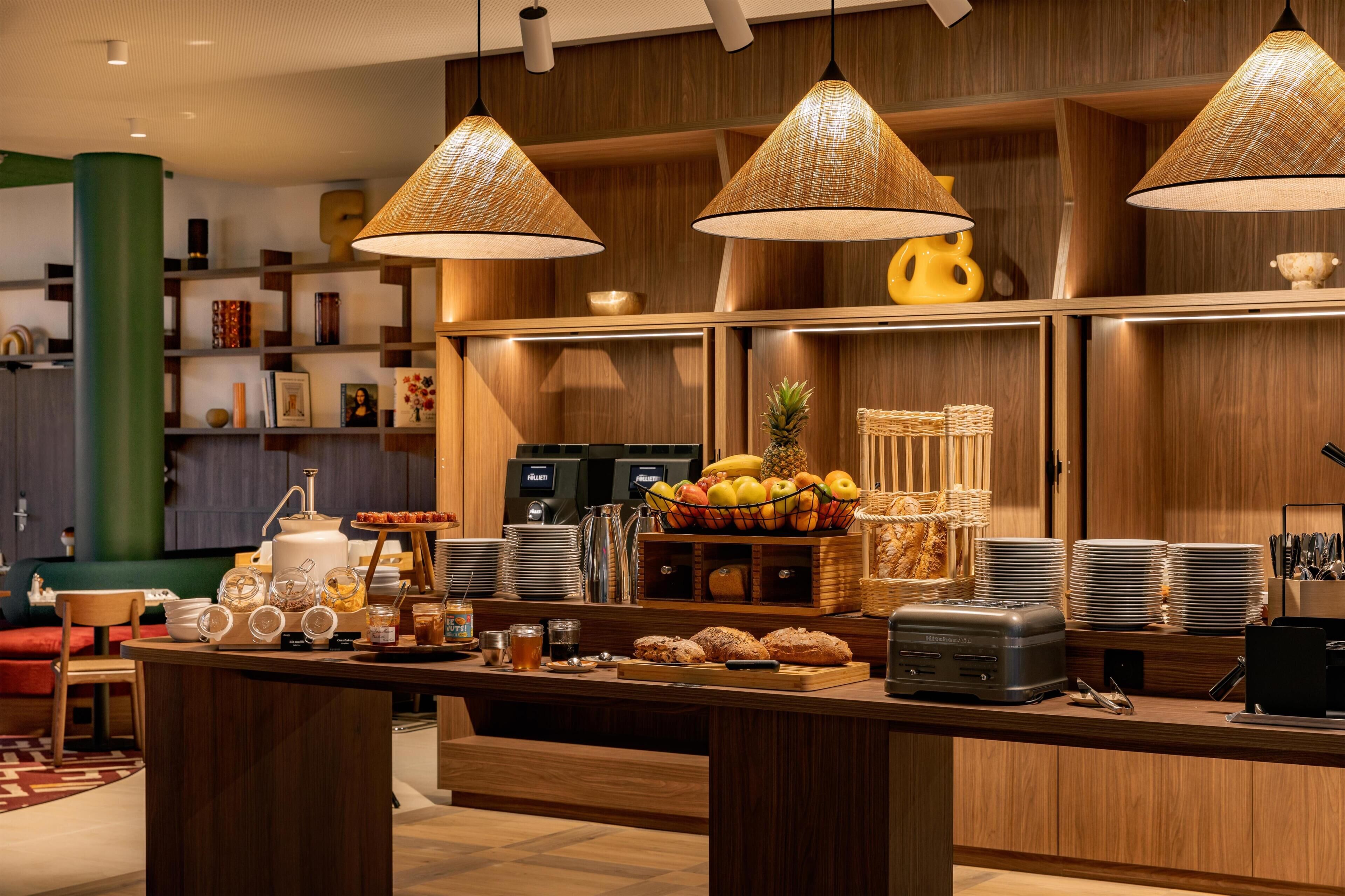 A well-lit kitchen area with wooden cabinets, a fruit bowl, and a coffee station.