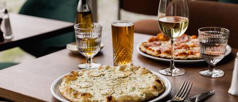 Un tavolo da pranzo con una pizza, un bicchiere di vino bianco e una pinta di birra.