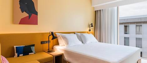 Une chambre d’hôtel avec un lit, une table de chevet, une lampe, un tableau et une vue sur l’extérieur.