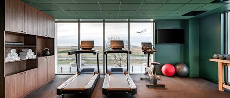 Une salle de sport équipée de tapis de course, de ballons d’exercice et d’une grande fenêtre donnant sur l’extérieur.