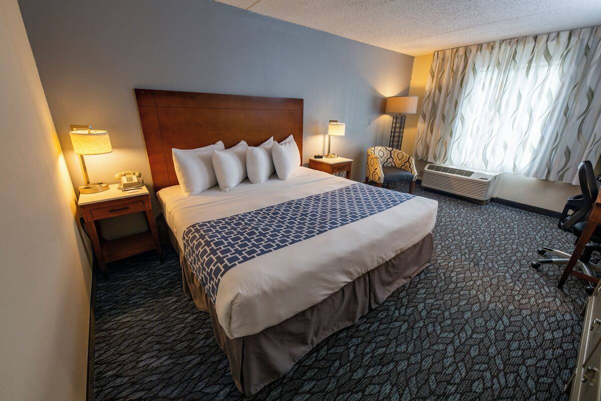 Une chambre d’hôtel avec un grand lit, deux tables de chevet avec des lampes, un bureau avec une chaise et une fenêtre avec des rideaux.