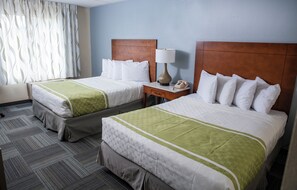 A hotel room with two beds, a nightstand with a lamp, and a telephone.