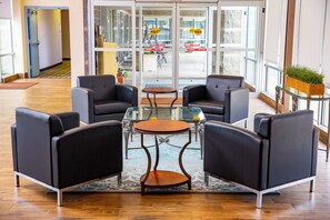 A lobby with a glass door entrance, a reception desk, and seating area with two round tables and four chairs.