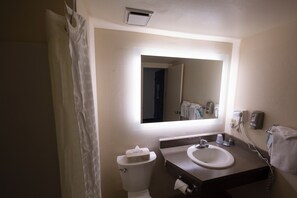 A bathroom with a toilet, sink, and mirror. - Hope Hotel & Conference Center (Dayton)