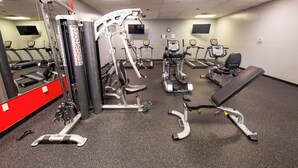A gym with various exercise machines, a mirror, and a clock on the wall. - Hope Hotel & Conference Center (Dayton)