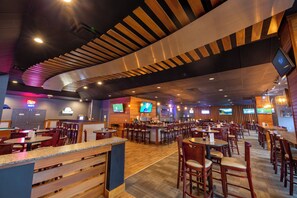 Un restaurant avec des poutres en bois au plafond, plusieurs écrans de télévision et un espace bar.