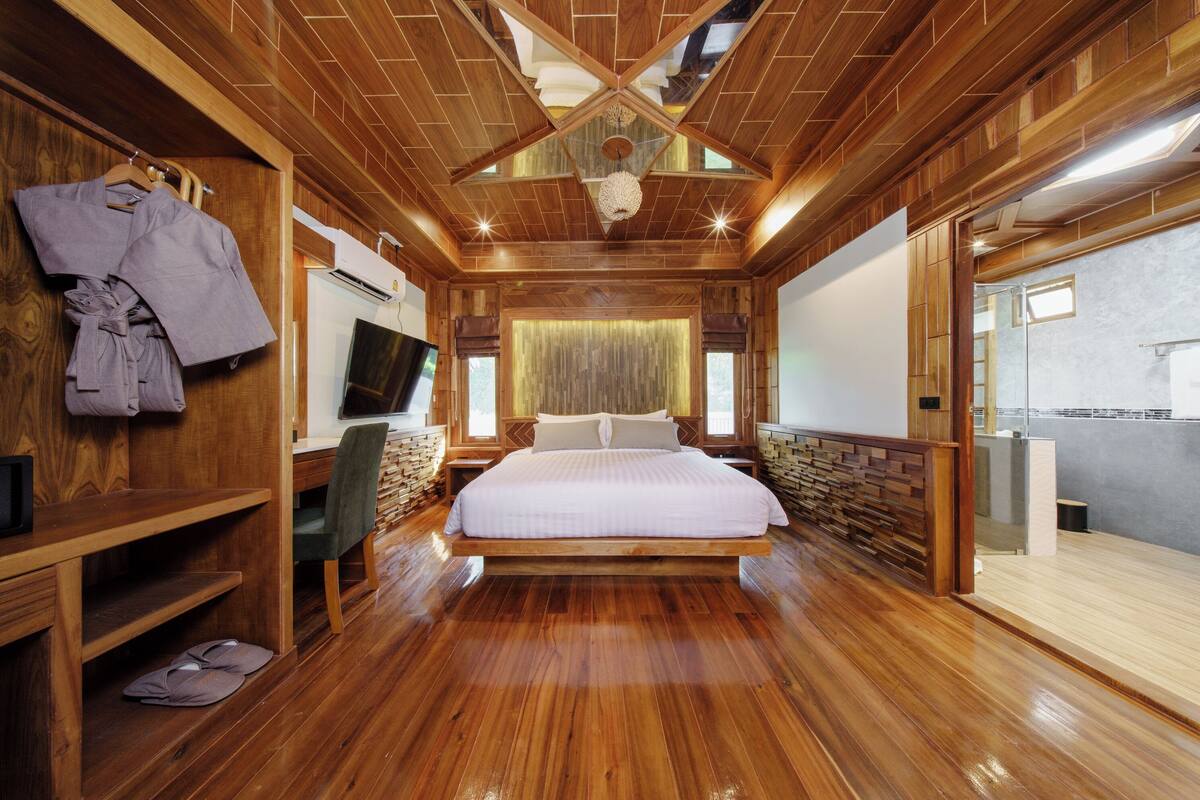 Un'ampia camera da letto con un letto grande, pareti in legno, una televisione e un bagno visibile attraverso una porta aperta.