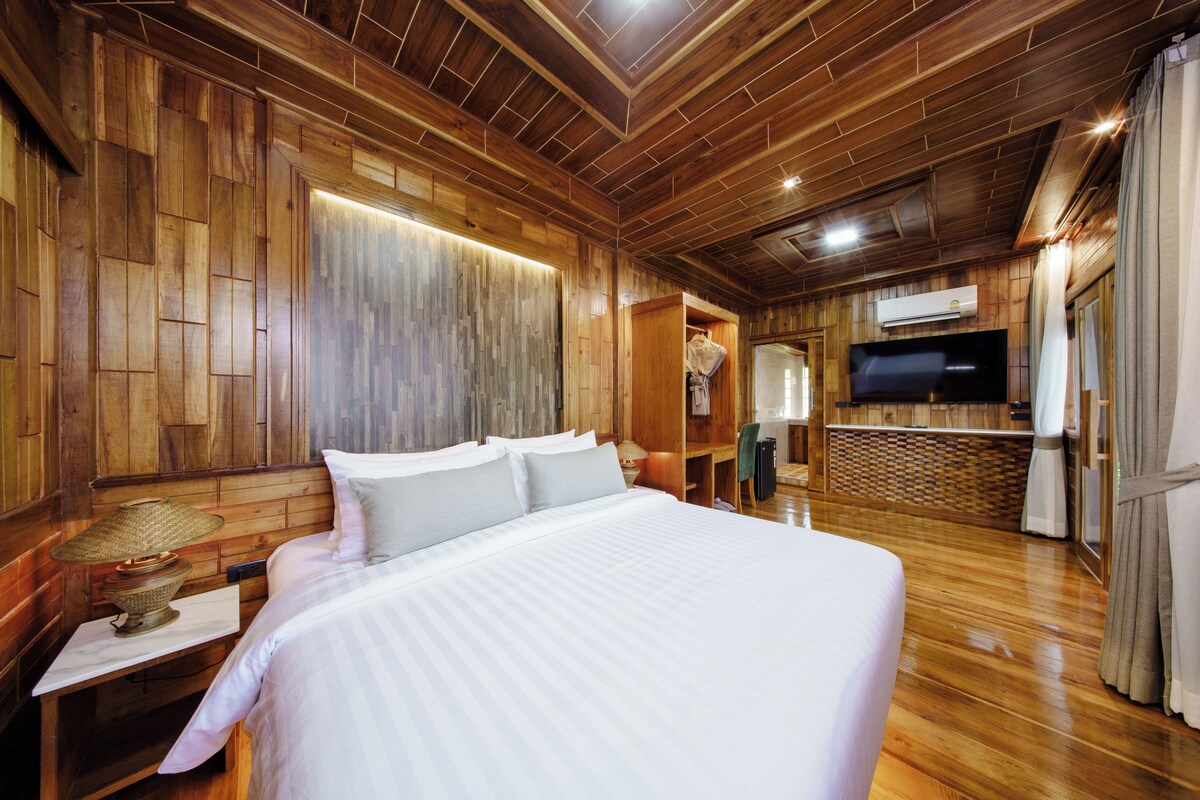 A wooden-paneled room with a large bed, a television, and a shower area.