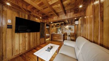 A wooden interior with a white sofa, a flat-screen TV mounted on the wall, and a small kitchen area.
