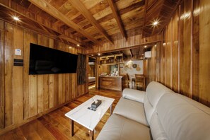 A wooden interior with a white sofa, a flat-screen TV mounted on the wall, and a small kitchen area. - Calisto Valley I Luxury Pool Villa Krabi (Krabi)