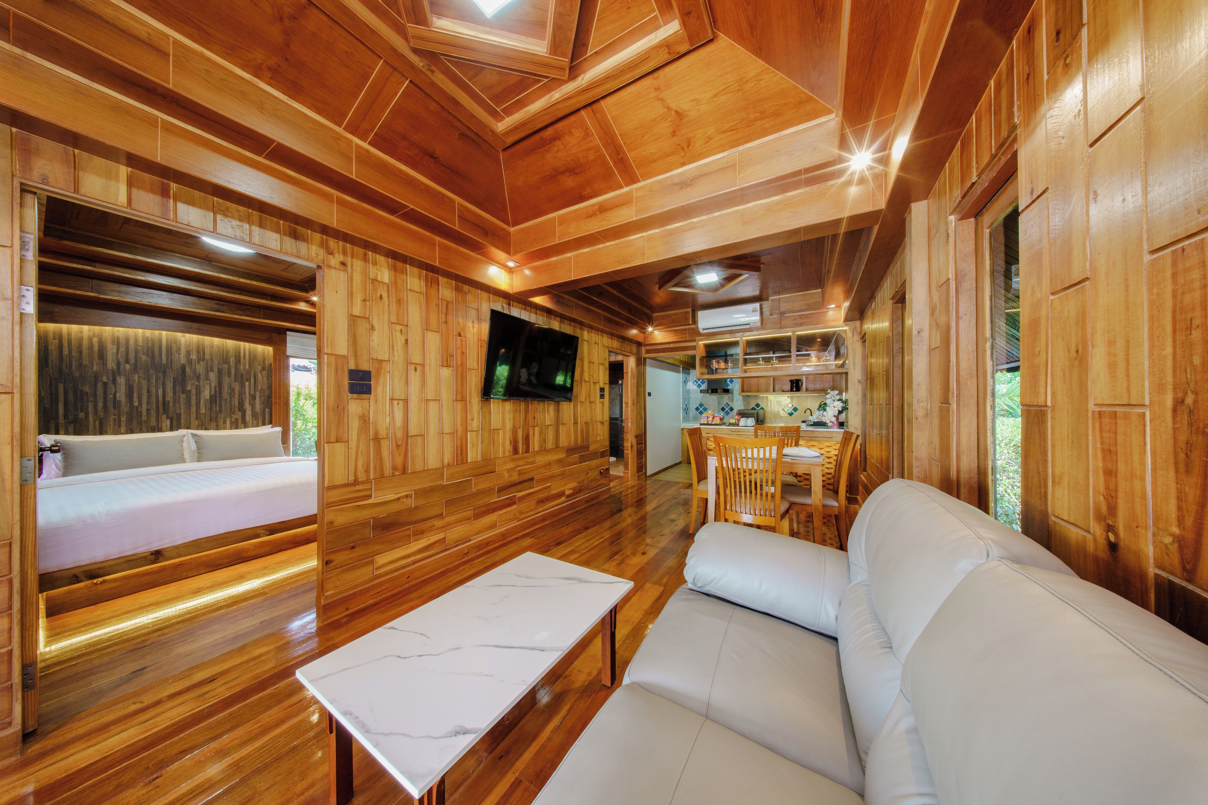 A wooden interior with a bed, sofa, dining area, and TV.