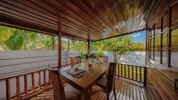 A wooden deck with a table set for dining, surrounded by chairs, and a view of tropical vegetation.
