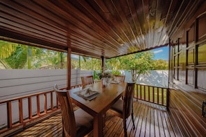 A wooden deck with a table set for dining, surrounded by chairs, and a view of tropical vegetation. - Calisto Valley I Luxury Pool Villa Krabi (Krabi)