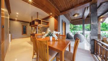 A spacious dining area with a wooden table and chairs, a white vase with flowers, and a view of lush greenery outside.