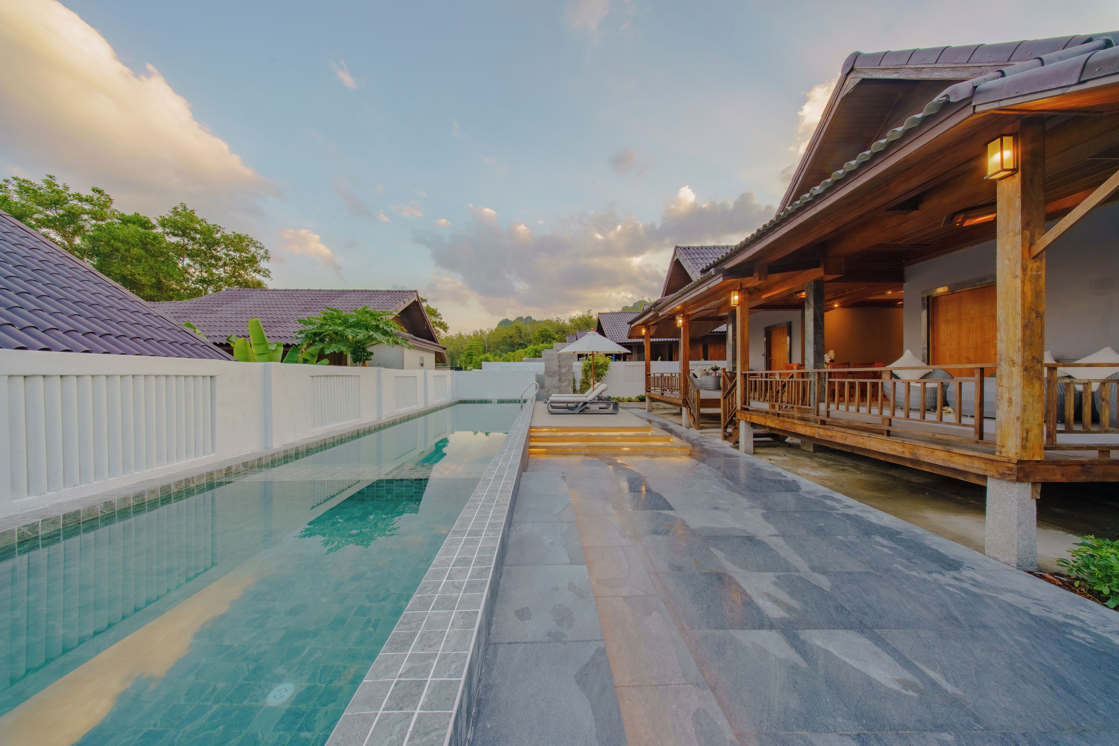 A swimming pool with a tiled deck, wooden deck with railings, and a covered area with seating.
