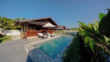 A swimming pool with lounge chairs and a wooden house in the background.