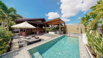 A swimming pool with a wooden deck and lounge chairs, surrounded by a wooden fence and palm trees.